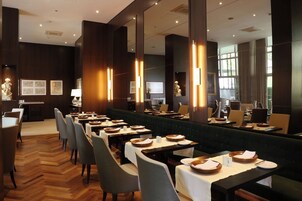A modern restaurant with long tables, dark wood paneling, and a green upholstered bench.