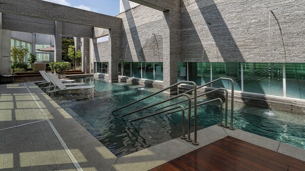 An indoor swimming pool with clear water, surrounded by stone walls and large windows. - Hotel Cadoro Sao Paulo (São Paulo)
