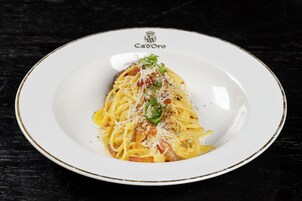 Lautasella on spagettia, juustoa ja vihreää koristetta. Lautanen on valkoinen ja siinä on kultainen reunus.