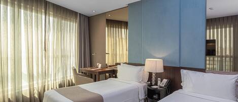 A hotel room with two beds, a desk, a chair, a lamp, and a phone.