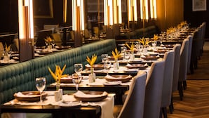 A restaurant with a long green upholstered bench seating, tables set with plates, glasses, and vases with yellow flowers. - Hotel Cadoro Sao Paulo (São Paulo)