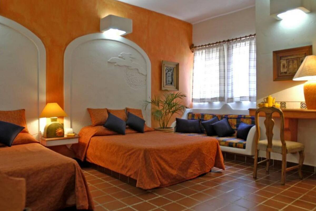 Quarto de hotel com duas camas, um sofá, uma poltrona e uma mesa.