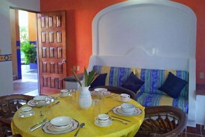 A dining area with a yellow table set for four, a white vase with a plant, and a sofa with blue cushions.