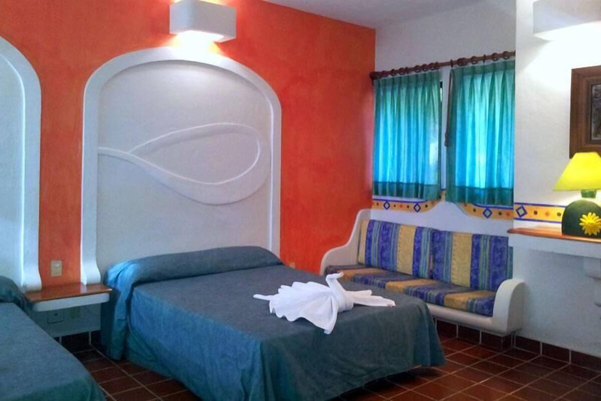 Quarto de hotel com cama, sofá, janela com cortinas e luminária.
