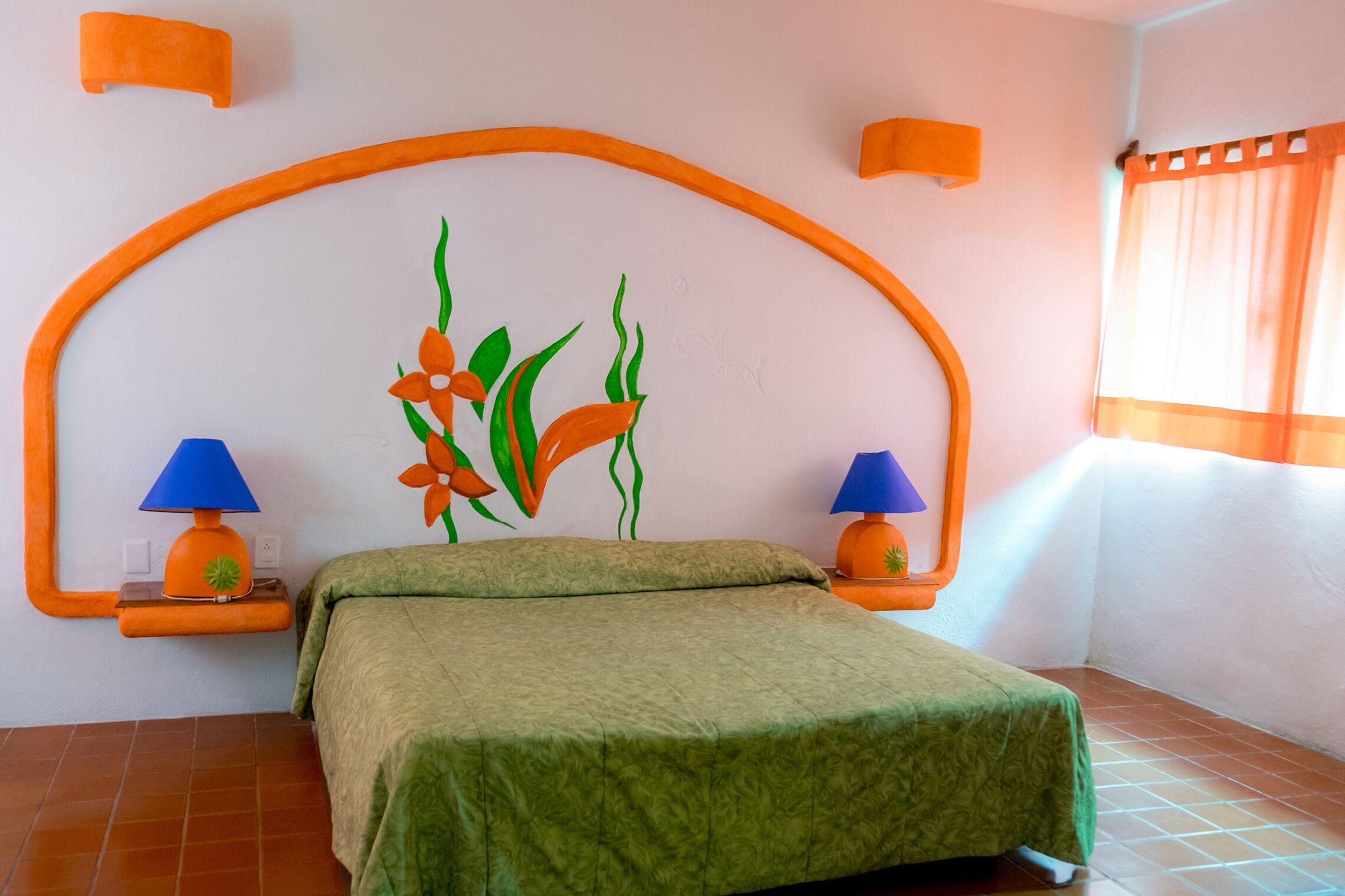 A bedroom with a bed, two lamps, a wall-mounted shelf, and a window with curtains.