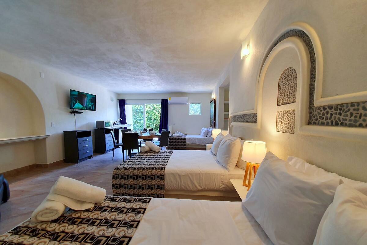 Quarto de hotel com cama, escrivaninha, televisão e vista para o verde.