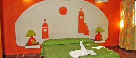 A hotel room with a large bed, green bedding, two wall-mounted lamps, and a mural with a sun and buildings.