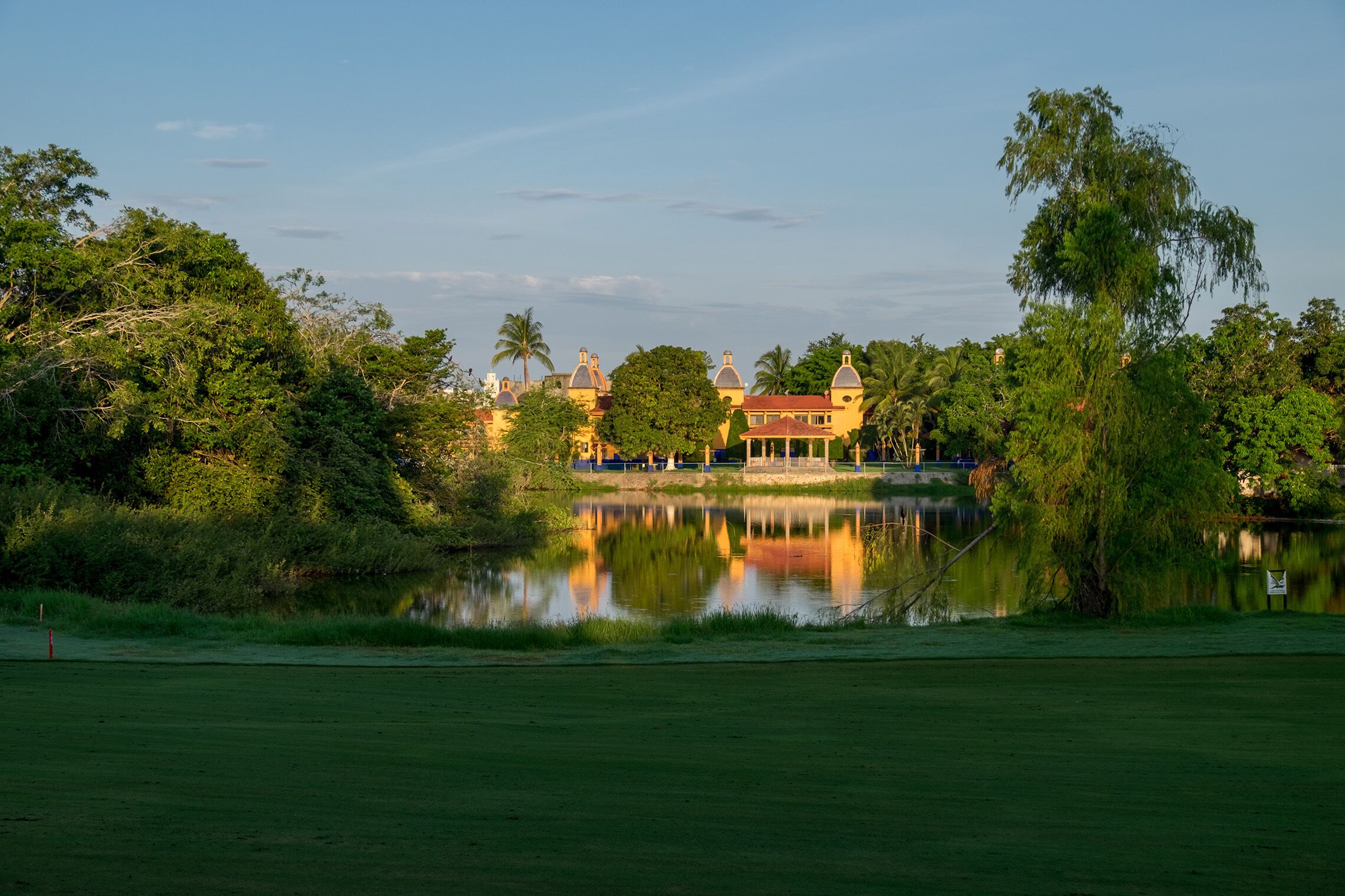A serene lakeside view with a building featuring domed roofs and a well-maintained lawn.