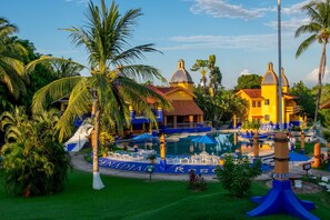 Un resort con piscina, palmeras y un edificio de fachada amarilla.