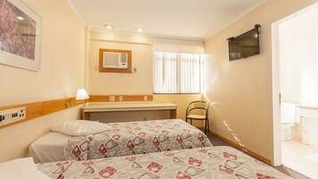 Une chambre d’hôtel avec deux lits, un bureau, une chaise, une télévision et une salle de bain visible à travers une porte ouverte.
