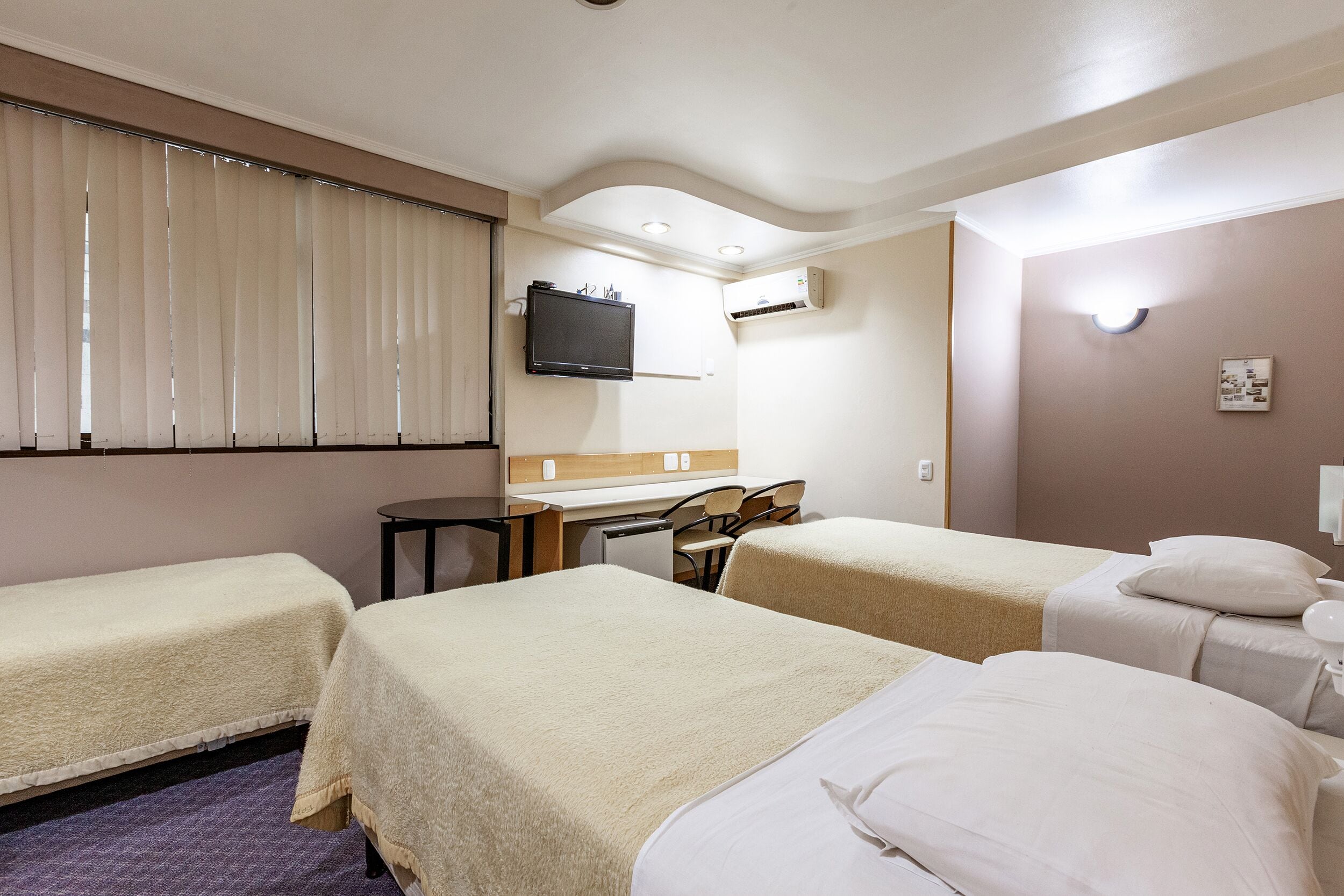 A hotel room with two single beds, a desk, a chair, a television, and an air conditioning unit.