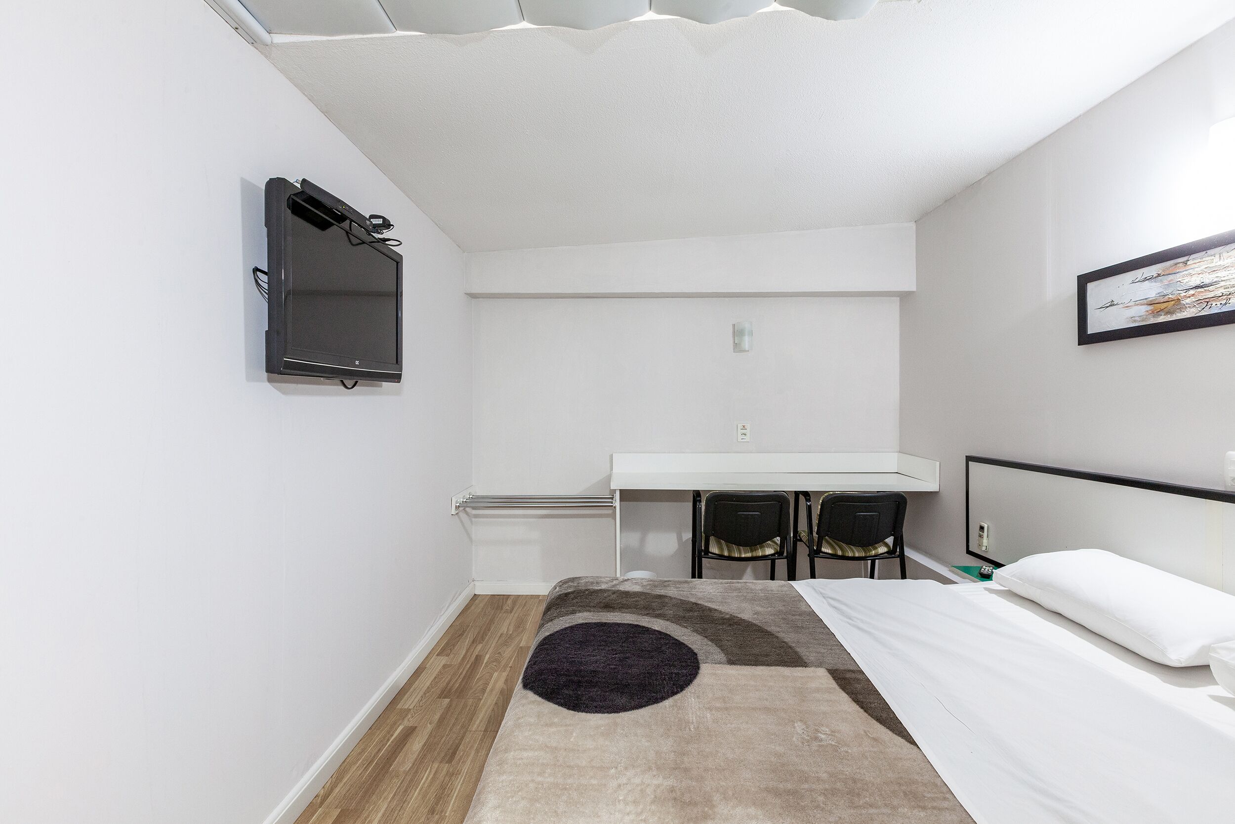 A small, modern room with a bed, a desk, and a chair.