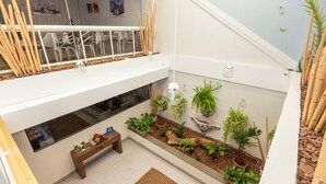 Un espacio interior amplio con un banco de madera, plantas en macetas y un ventanal con vistas a un comedor.