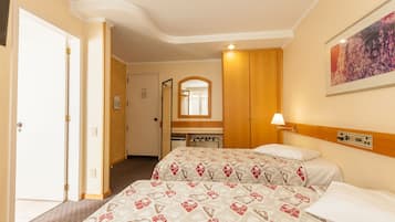 Habitación de hotel con dos camas, un armario de madera, un espejo y un cuadro en la pared.