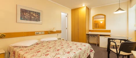 A hotel room with a bed, a desk, a chair, a mirror, and a painting on the wall.
