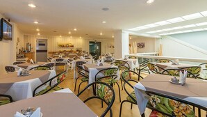Un comedor con mesas y sillas, una cocina al fondo y una escalera que sube a un nivel superior.