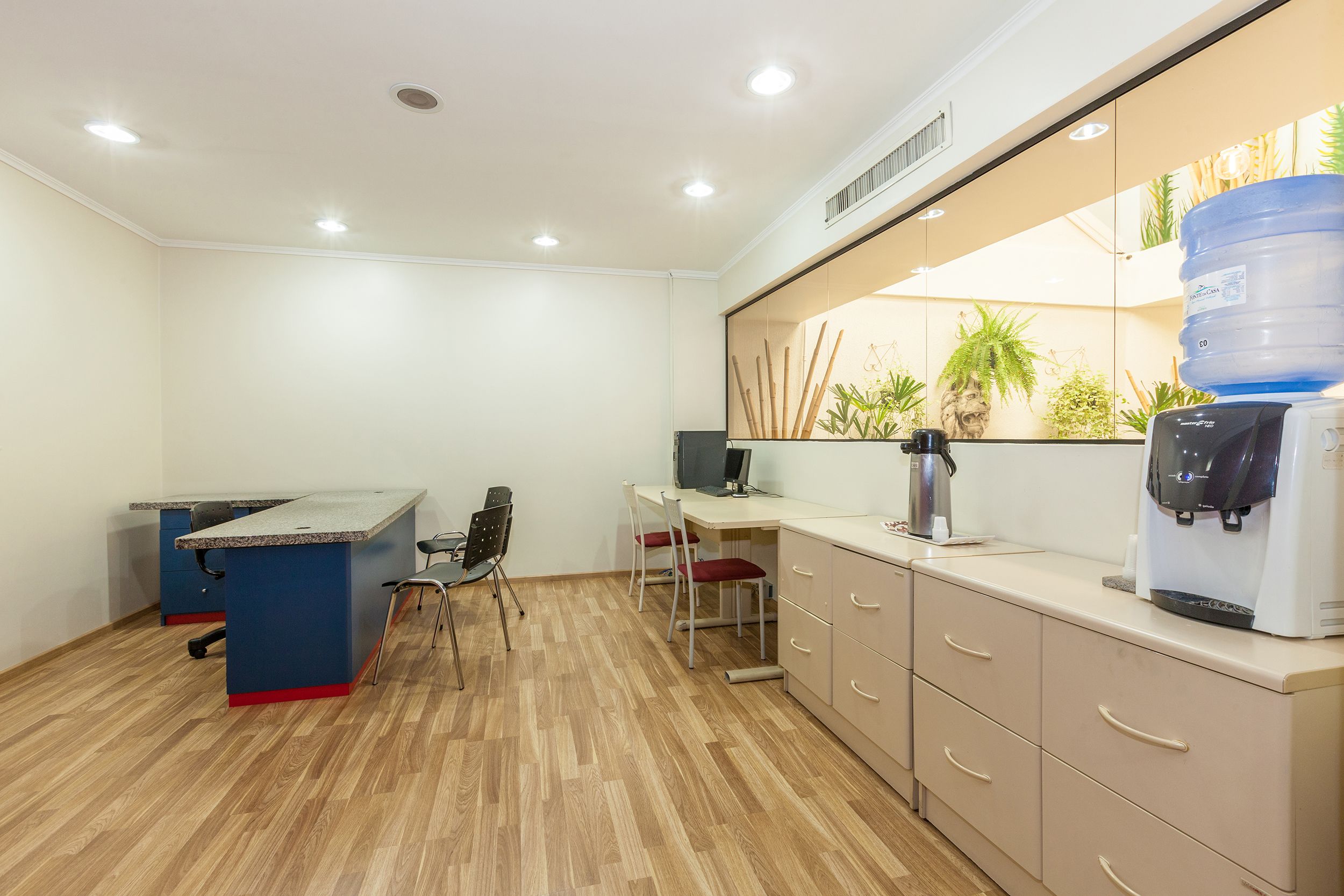 Un espacio de oficina moderno con un escritorio azul, dos sillas, una computadora y un dispensador de agua.