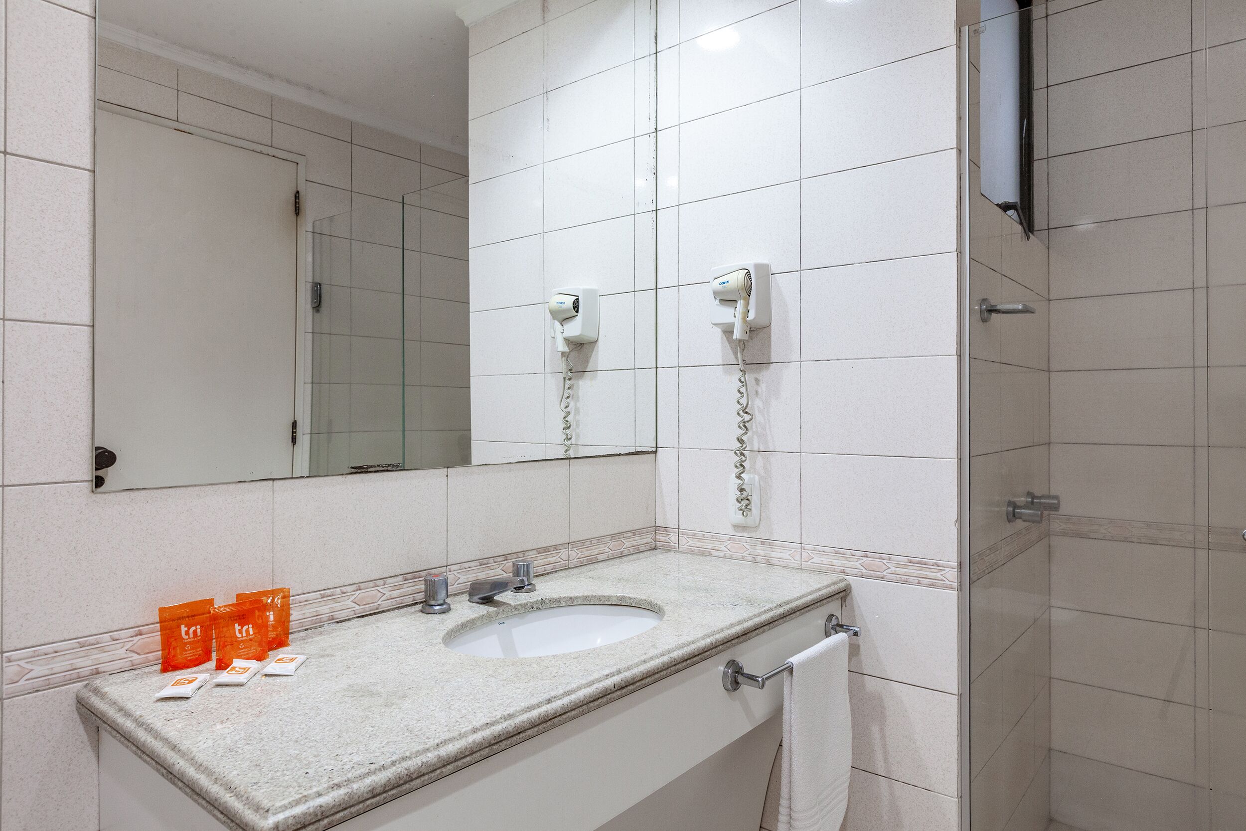 A bathroom with a sink, mirror, and two hair dryers mounted on the wall.