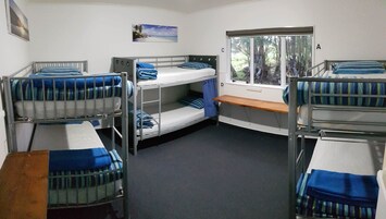 Un dormitorio con literas, una ventana que da a árboles y un escritorio pequeño.