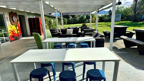 Een terras buiten met een witte tafel en blauwe stoelen, omgeven door groen en uitzicht op het landschap.
