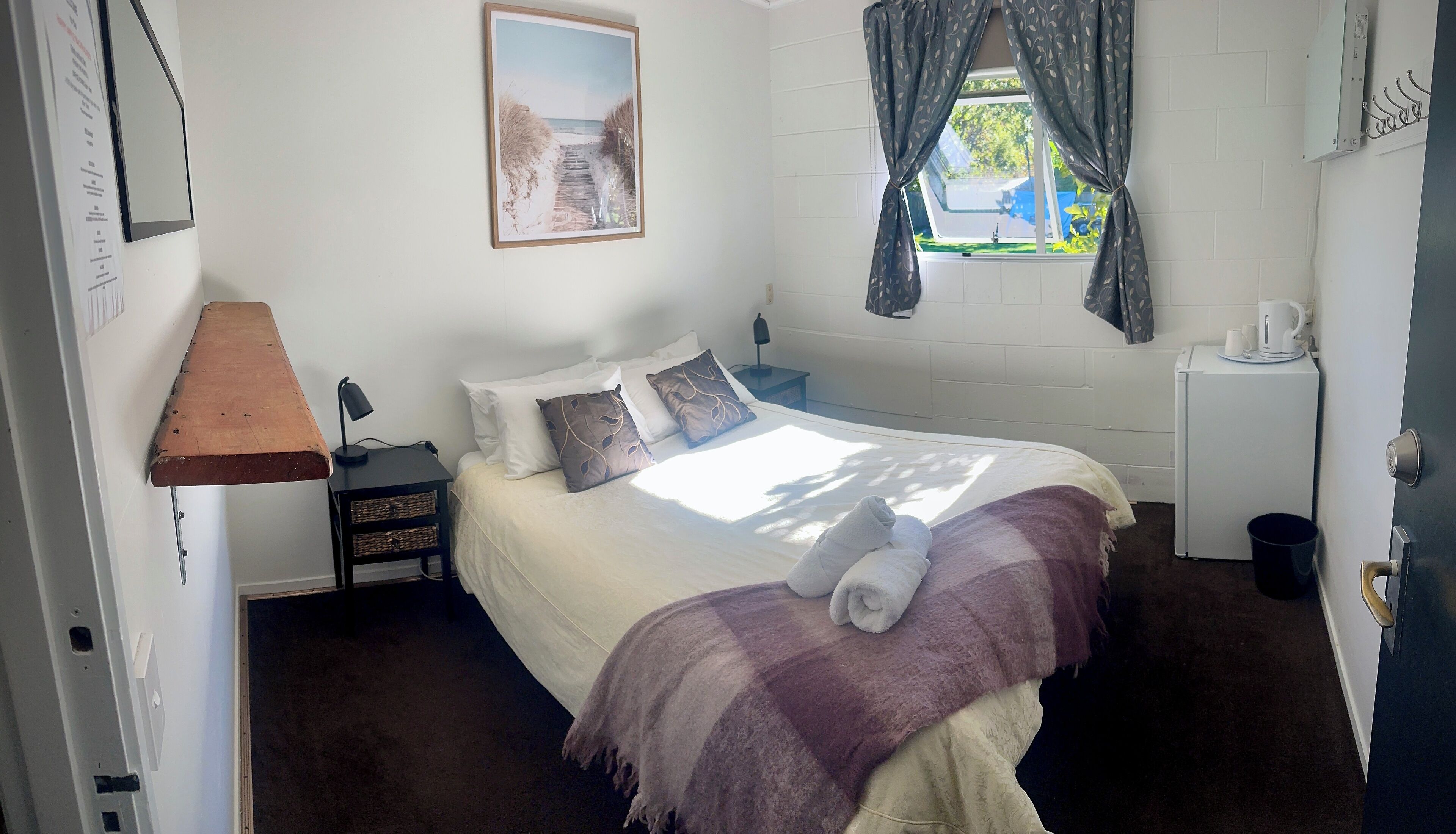 Een slaapkamer met een bed, nachtkastjes, een lamp, een ingelijst schilderij aan de muur en een raam met gordijnen.