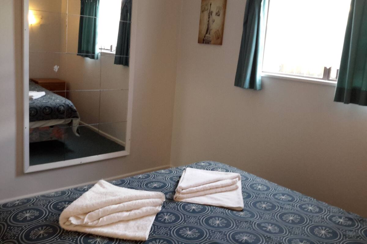 Une chambre à coucher avec un lit, un miroir, une fenêtre avec des rideaux et un tableau accroché au mur.