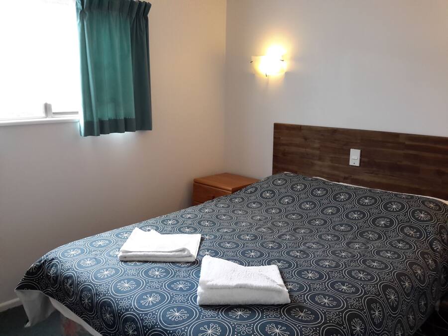 A neatly made bed with a patterned bedspread, a wooden headboard, a bedside table, and a wall-mounted light fixture.