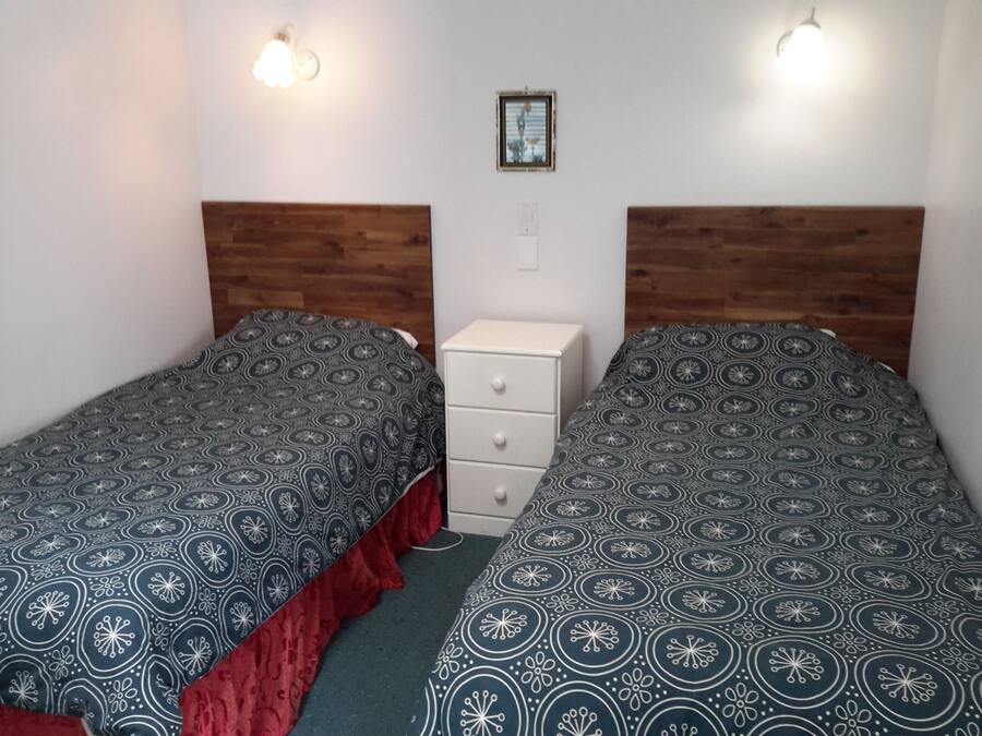 A room with two single beds, each with a patterned bedspread and a wooden headboard. There is a small white dresser between the beds.