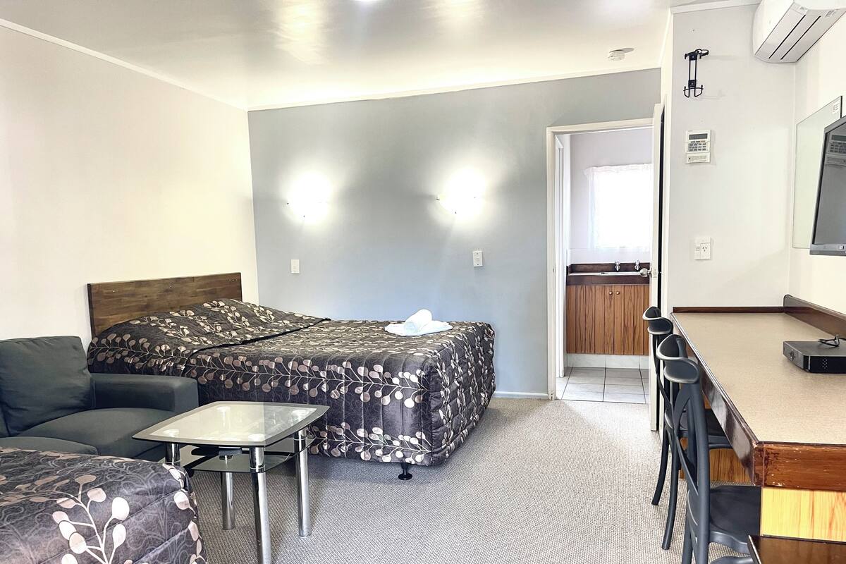 Une chambre d’hôtel comprenant un lit, un canapé, une petite table, un bureau avec des chaises et une kitchenette.
