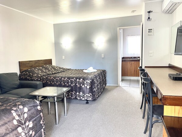Een hotelkamer met een bed, een slaapbank, een tafeltje, een bureau met stoelen en een kitchenette.