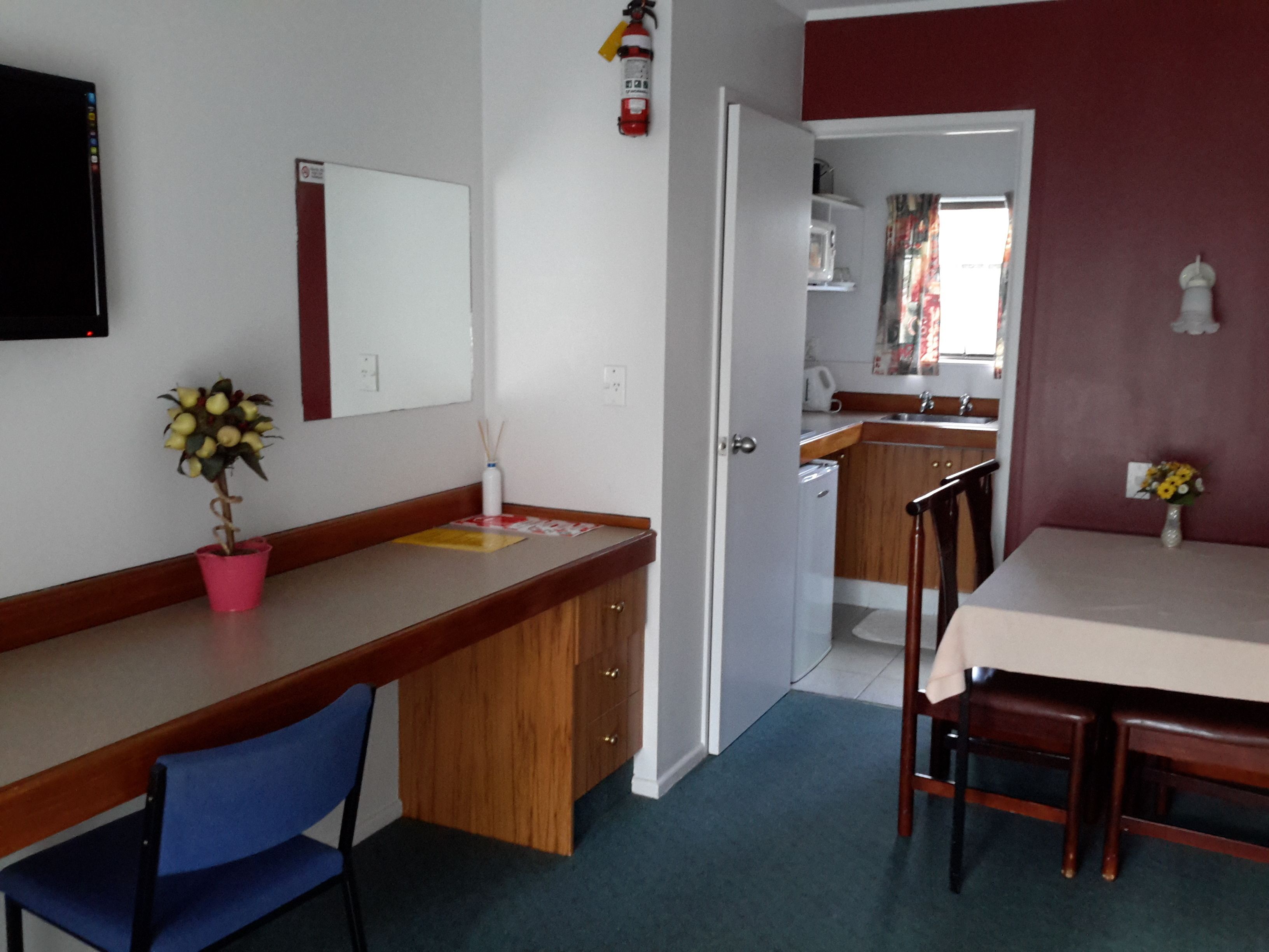 Cocina compacta con microondas, lavabo y armarios. Se ve un comedor con una mesa y sillas, junto con una pequeña planta en maceta.