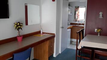 Cocina compacta con microondas, lavabo y armarios. Se ve un comedor con una mesa y sillas, junto con una pequeña planta en maceta.
