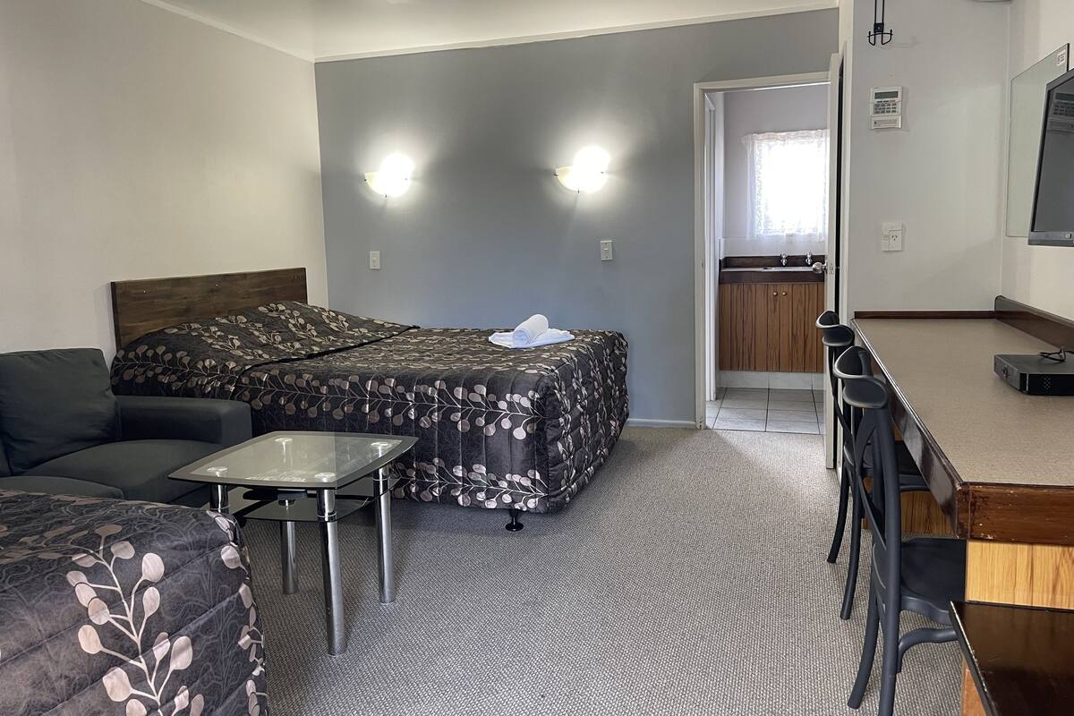 Une chambre d’hôtel comprenant un lit, un canapé, une petite table, un bureau avec des chaises, une kitchenette et un appareil de climatisation.