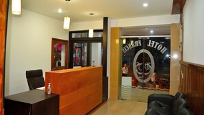 Zona de recepción de un hotel con un mostrador de madera, una silla de cuero negro y una puerta de cristal que muestra el nombre del hotel.