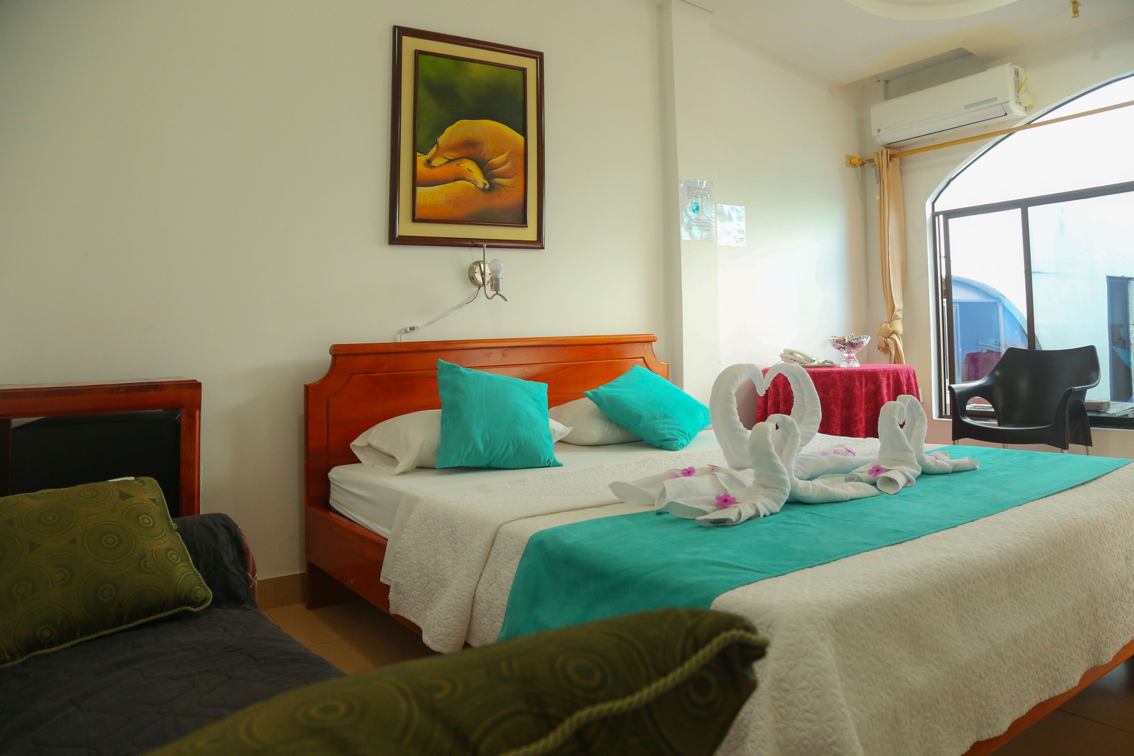 A hotel room with a bed, a chair, a table with a red tablecloth, and a window with curtains.