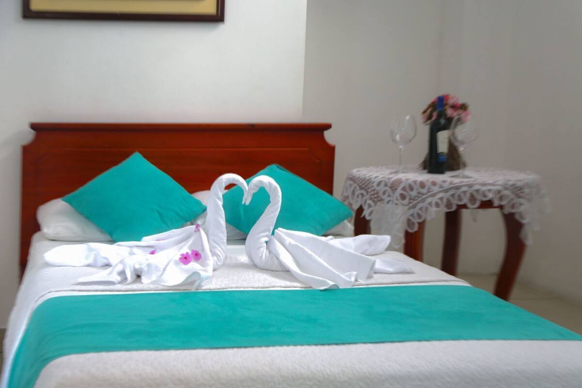 Uma cama bem arrumada com um cobre-leito verde-água, duas almofadas verde-água e um cobertor branco.
