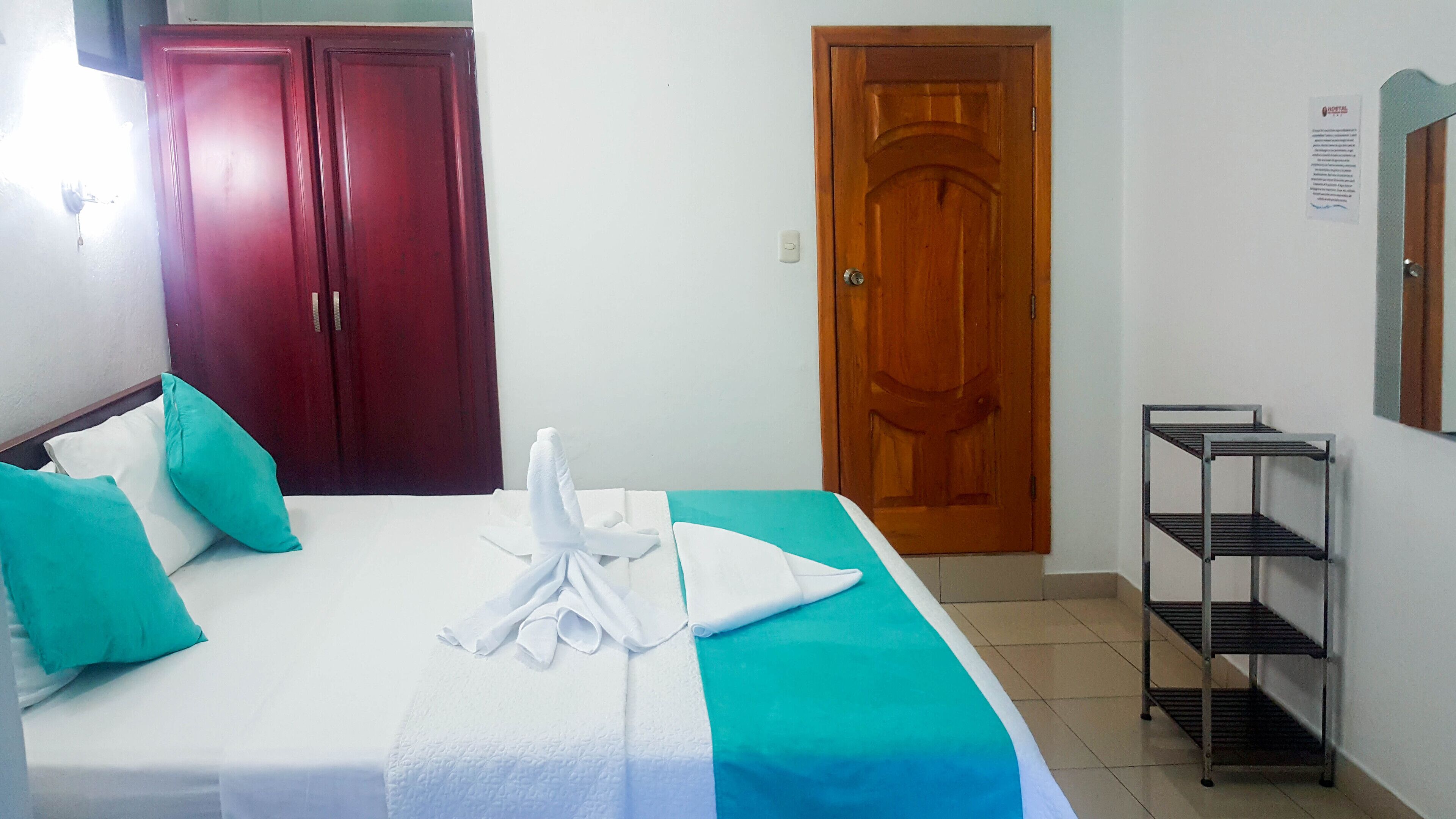 Ein Hotelzimmer mit einem Bett, zwei Türen, einem Regal und einem an der Wand befestigten Schild.
