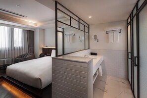 A modern hotel room with a large bed, a separate bathroom with a large mirror, and a small seating area. - Glad Live Gangnam (Seoul)