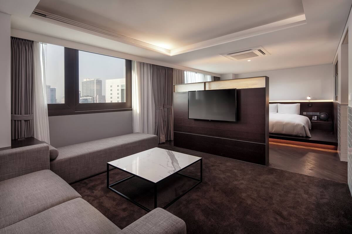 A modern hotel room with a large bed, a flat-screen TV, a sofa, and a coffee table.