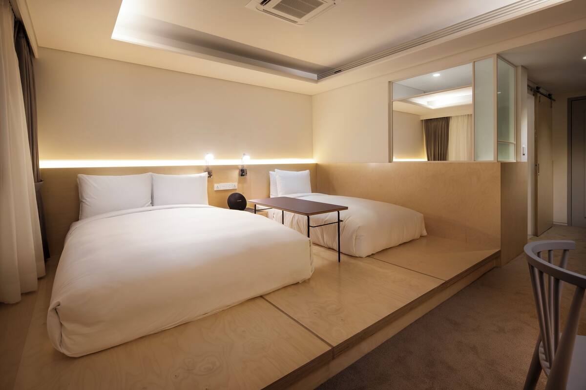 A modern hotel room with a large bed, a smaller bed, a desk, and a chair.
