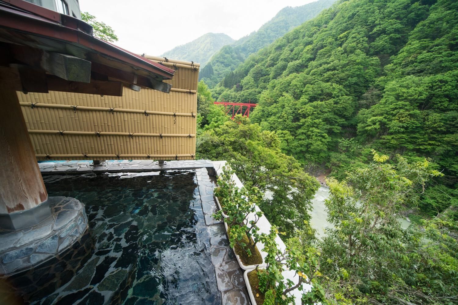 A traditional Japanese building with a stone water feature and a view of a lush green valley.