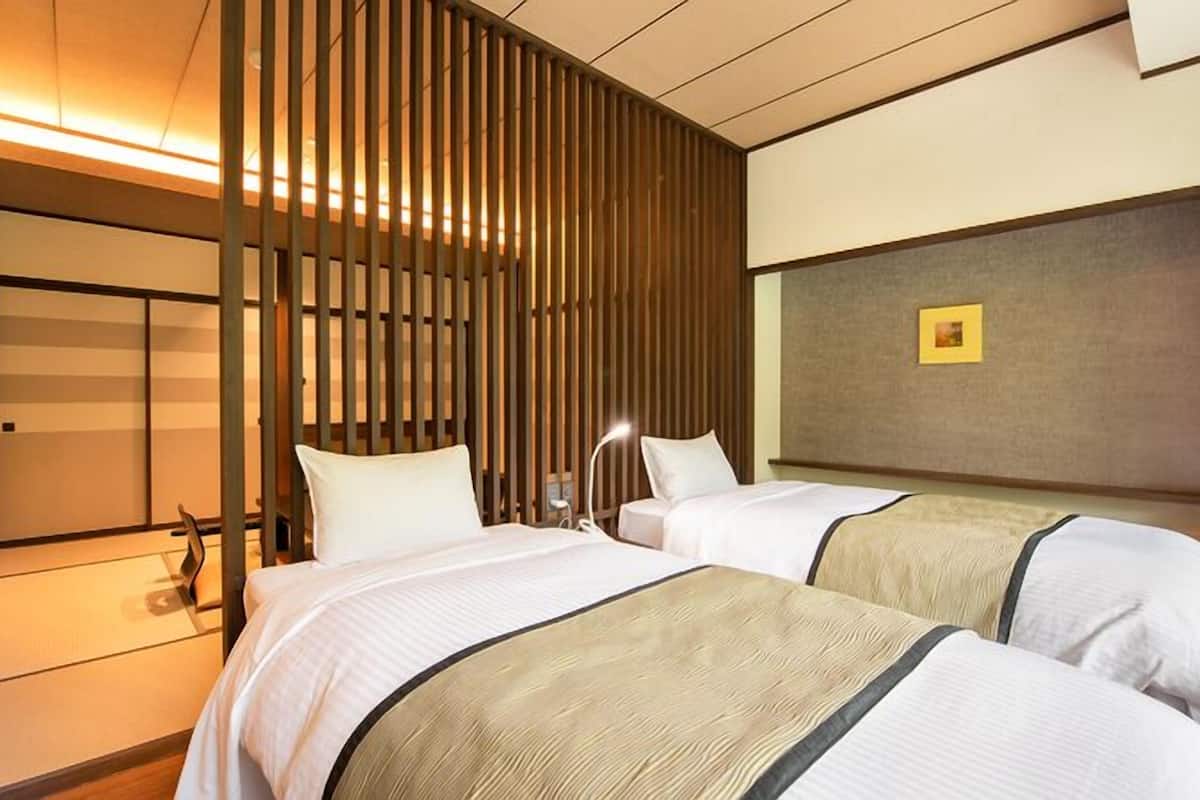 A hotel room with two beds, a wooden slat partition, a bedside table with a lamp, and a framed picture on the wall.
