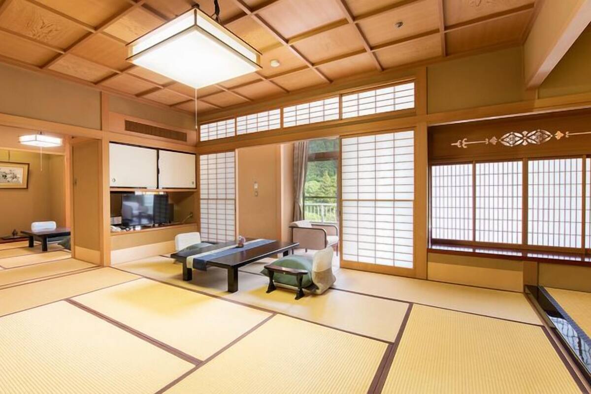 A traditional Japanese room with tatami flooring, a low table, a sofa, sliding doors, and a television.