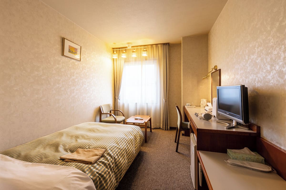 A hotel room with a bed, a desk with a computer, a chair, and a television.