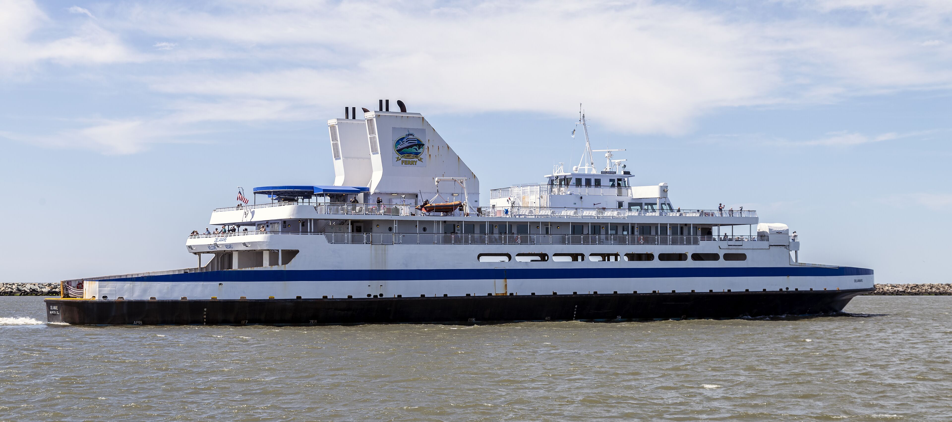 Un grand ferry avec plusieurs ponts et une bande bleue, naviguant sur l’eau.