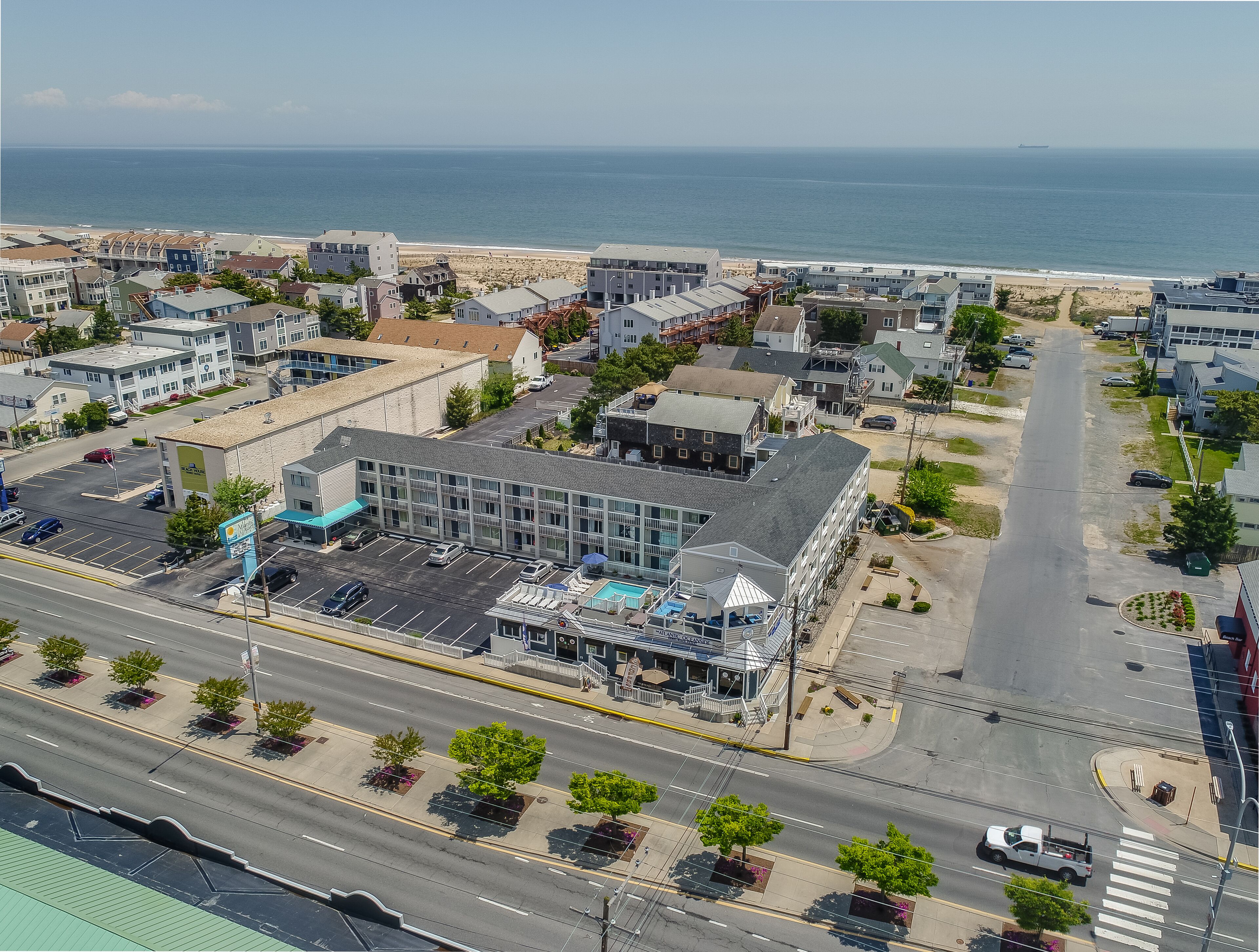 An aerial view of a coastal town with a prominent building featuring a swimming pool and a beach in the background.