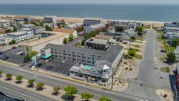 An aerial view of a coastal town with a prominent building featuring a swimming pool and a beach in the background.