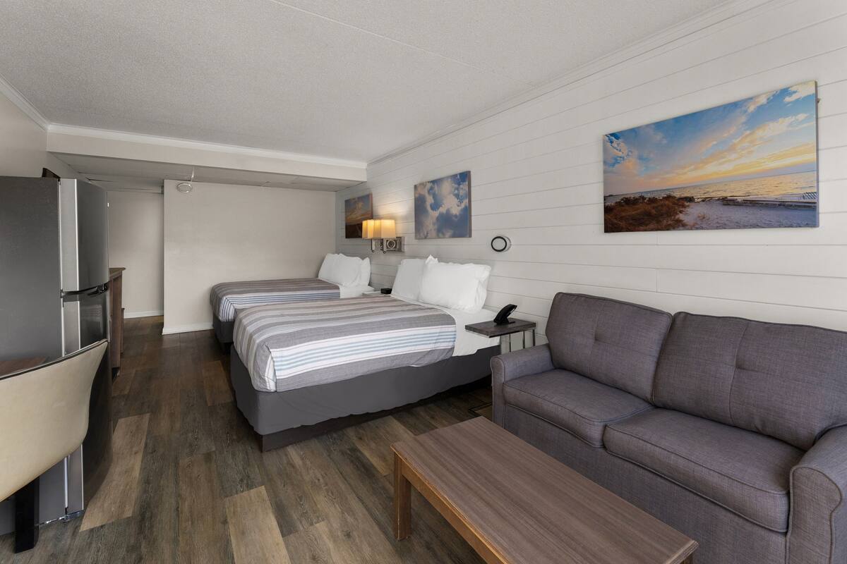 A modern hotel room with a bed, a sofa, a desk, and a TV.