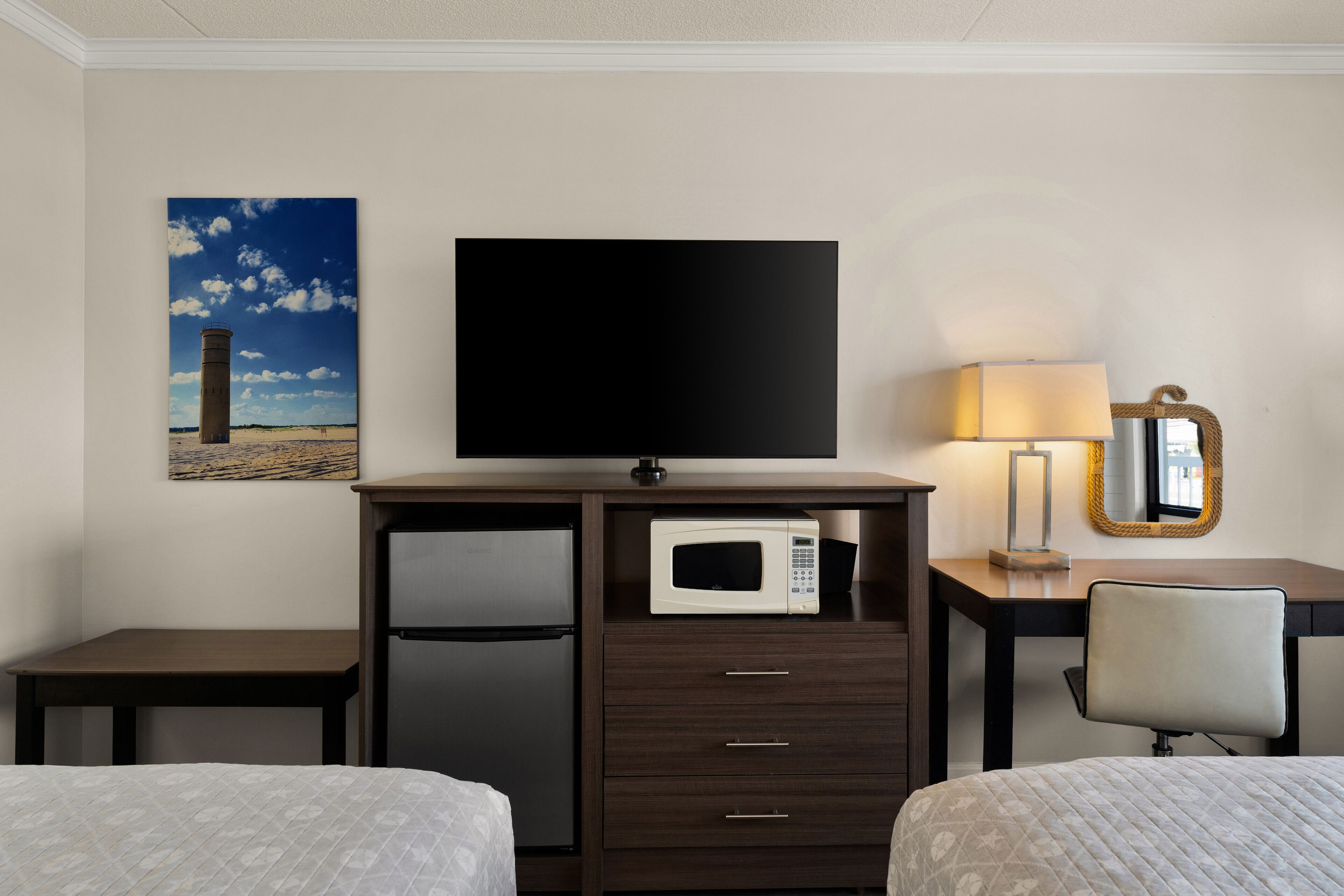 Habitación de hotel con cama, escritorio con microondas, televisor, lámpara y espejo.