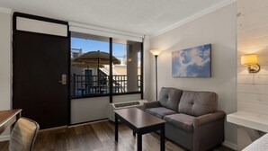 A hotel room with a sofa, a small table, a bed, a window with a view of the outside, and a wall-mounted lamp. - Atlantic Oceanside Dewey (Dewey Beach)